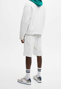 Vit denimjacka och shorts, i bomullsblandning. Teal huva sweatshirt under. Vita sneakers med grå detaljer. Randiga vita strumpor.