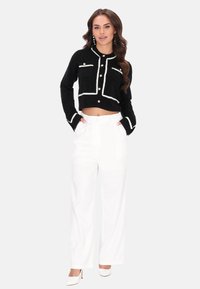 Fekete, fehér díszítéssel ellátott, cropped dzseki, elülső zsebbel és arany gombokkal, magasan derekú fehér nadrággal és hegyes orrú fehér magassarkú cipővel párosítva.