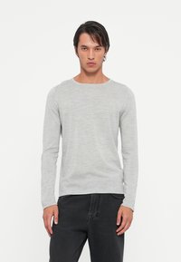 T-shirt à manches longues gris clair en tissu lisse. Doté d'un col rond et d'une coupe ajustée. Design minimaliste avec une texture subtile.