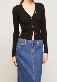 Czarny kardigan z prążkowanym wzorem, z dekoltem w serek i pięcioma złotymi guzikami, w zestawieniu z niebieską spódnicą dżinsową z wysokim stanem.