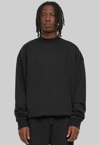Sweatshirt noir oversize, col rond, épaules tombantes, poignets côtelés, texture douce, design minimaliste, associé à un pantalon noir assorti.