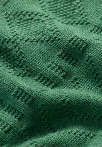 Zaļš adīts audums ar teksturētu rakstu. Virsma rāda dažādus zaļās krāsas toņus, radot smalku dziļumu un mīkstumu.