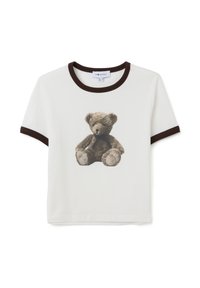 Camiseta blanca de manga corta con ribete marrón y un oso de peluche marrón impreso con un lazo negro en la parte delantera.
