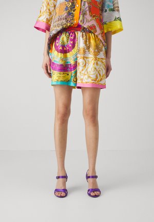 Colorful silk top with patterned design, paired with brightly patterned shorts. Worn with purple strappy heels, featuring a sleek design.