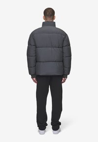 Jachetă puf gri cu guler înalt, segmente rectangulare și o croială lejeră, asortată cu pantaloni negri și adidași albi.