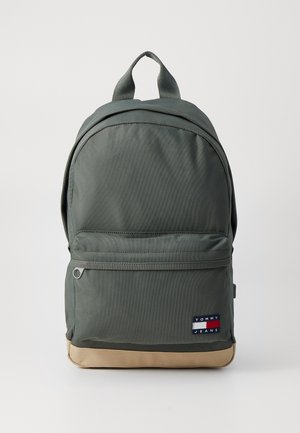 Ciemnozielony plecak z materiału z beżowym spodem, przednią kieszenią na suwak, górnym uchwytem i naszywką z logo Tommy Jeans na przedniej kieszeni.