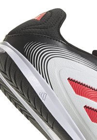 Närbild av en svart, vit och röd sportskosula med texturerat mönster och böjda randmönster på sidan.