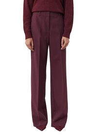 Woman wearing high-waisted, wide-leg plum-colored trousers with matching pointed shoes and a textured knit sweater.