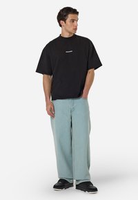 Čierne oversize tričko s logom "PEGAADOR". Svetlo modré široké nohavice. Čierne tenisky s textúrovaním. Jednoduchý a moderný dizajn.