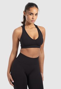 Sujetador deportivo negro con un escote en V profundo y tirantes dobles, combinado con leggings negros de cintura alta, ambos en una tela suave y elástica.