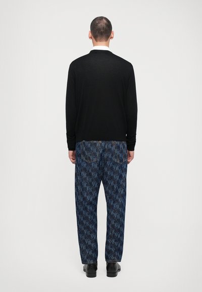 Black knit sweater and blue denim jeans featuring a bold, repeating logo pattern. The jeans have contrasting stitching and back pockets.