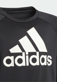 Czarna koszulka sportowa wykonana z gładkiego materiału, z dużym białym logo Adidas oraz trzema ukośnymi paskami na lewej części klatki piersiowej.