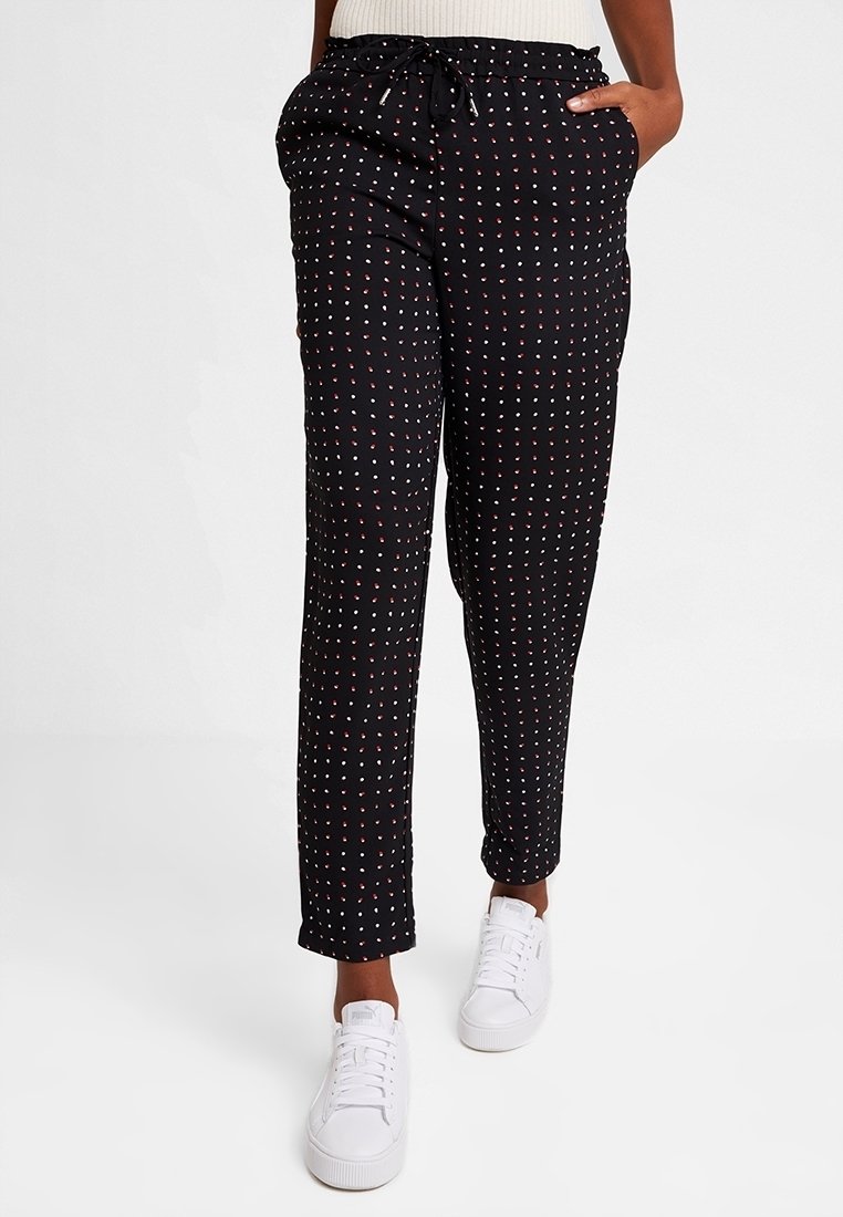 Pantalon noir léger avec une taille à cordon, présentant un motif de petits pois rouges et blancs ; porté avec des baskets blanches.