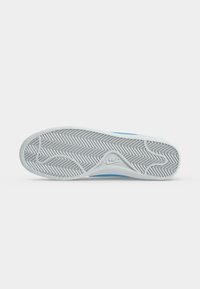 Η σόλα ενός λευκού αθλητικού παπουτσιού Nike με μοτίβο ψαροκόκαλου και το λογότυπο της Nike στο κέντρο, σε απλό ανοιχτό γκρι φόντο.