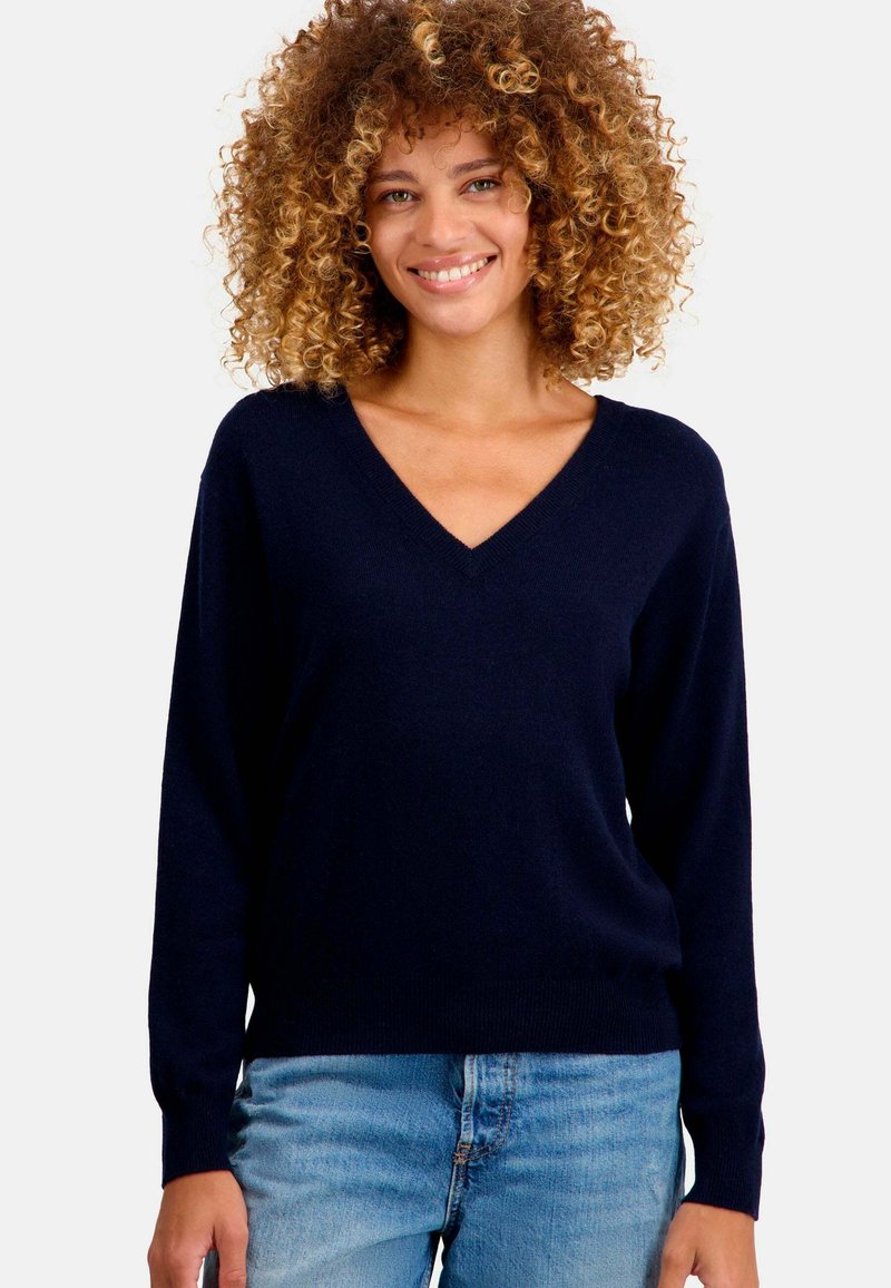 Pull bleu marine à col en V en tissu tricoté doux avec des manches longues, présentant une coupe décontractée et des poignets et un ourlet côtelés, associé à un jean bleu clair.