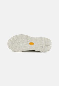 Potplat sportske obuće, izrađen od teksturirane bijele gumene tvari s višesmjernim izbočinama za prianjanje. Vibram logo u žutoj boji blizu središta.