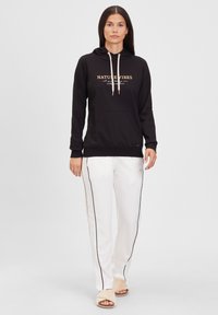 Sudadera negra con "NATURE VIBES" impreso en dorado, con cuello de cordón y bolsillo frontal. Combinada con pantalones blancos que tienen franjas laterales negras.