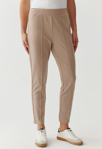 Lichtbeige taps toelopende broek met een elastische tailleband, met zijnaad en een gladde textuur, gecombineerd met witte en tan sneakers.