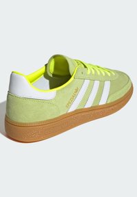 Gröna mockasneakers med vita ränder, gummisula och neongula accenter. Har en vadderad krage och en strukturerad gummisula.