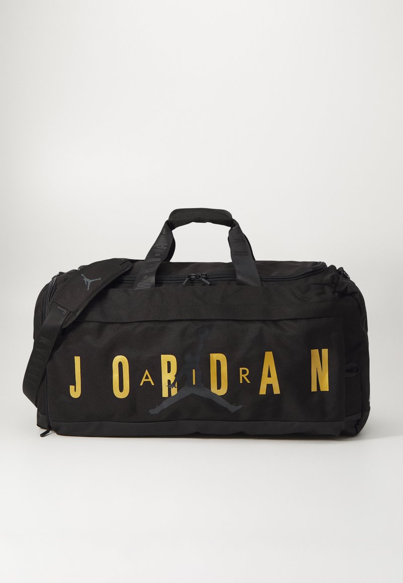 Melnā sporta soma ar zeltītu "JORDAN" nosaukumu. Sagezēts ievērojams melns Jumpman logo, divas augšējās rokturis un regulējama siksna.