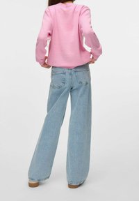 Różowy sweatshirt z długimi rękawami, w połączeniu z jasnoniebieskimi szerokimi spodniami dżinsowymi. Spodnie mają tylne kieszenie i wyblakłą teksturę dżinsu.