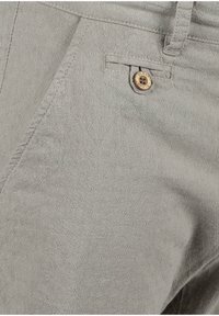 Ljust grå tygbyxor med ett texturerat mönster av små diamantformer, accentuerade av en träknapp och subtila sömnadsdetaljer.