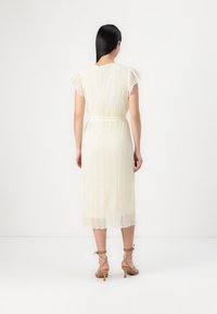 Robe midi blanche en dentelle avec de courtes manches volantées, taille cintrée et texture à motifs. Présente un ourlet superposé et est portée avec des talons à bride cheville beiges.