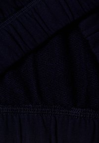 Námornická modrá látka s texturovaným pletením a hladkými částmi. Obsahuje detail s gumičkou a nabíráním. Měkký, lehký materiál se jemným leskem.