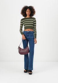 Grønn og hvit stripete kortermet strikkegenser, blå høy midje bootcut jeans, holder en burgunder kurvet håndveske, svarte platform sandaler.