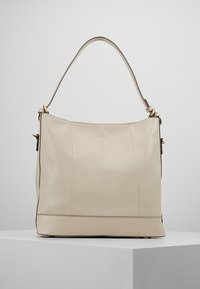 Krämfärgad läderhandväska med slät yta, som har ett enda axelband och subtila guldfärgade accenter. Fyrkantig botten och minimala sömmar.