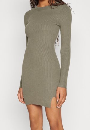 Dopasowana, prążkowana sukienka z długim rękawem w oliwkowym kolorze, z niewielkim rozcięciem z przodu, noszona przez osobę od ramion do połowy uda na jednolitym tle.