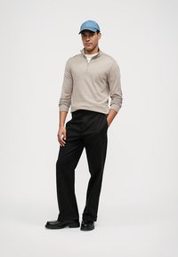 Pulover bej cu fermoar la jumătate, pantaloni negri și o pălărie bleu deschis. Această ținută are o croială lejeră, cu un design simplu și culori uniforme.