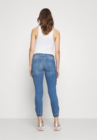 Ljusblå denim-joggers med uppvikta anklar, sidofickor och smal passform, tillsammans med en vit linne och beige skor.