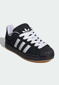 Čierna semišová teniska s tromi bielymi pruhmi, gumovou špičkou a bielymi šnúrkami. Vrchná časť má textúru a podrážka je svetlohnedá.