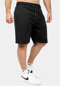 Pantaloni corti neri in cotone con vita elasticizzata, cordoncino e tasche laterali. Presentano una vestibilità comoda e si fermano sopra il ginocchio.