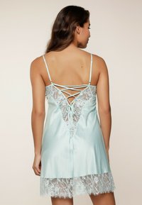 Vestaglia in raso blu chiaro con dettagli in pizzo, caratterizzata da un design della schiena in pizzo, spalline regolabili e orlo in pizzo a ondine.