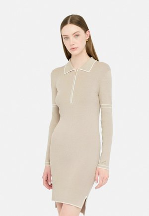 Abito beige a coste con maniche lunghe, colletto e una cerniera a metà. Caratterizzato da rifiniture bianche e fessure laterali per un tocco di dettaglio e texture.