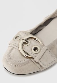 Bailarinas de ante gris claro con punta redondeada, detalles cosidos y una hebilla circular metálica con dos ojetes en la correa.