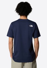 Dunkelblaues Baumwoll-T-Shirt mit kurzen Ärmeln und Rundhalsausschnitt. Es hat einen weißen Logodruck auf dem oberen Rücken und einen lockeren Schnitt.