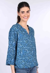 Hellblaue Bluse mit Blumenmuster, V-Ausschnitt und drei Viertelärmel, gefertigt aus leichtem Stoff mit filigranen botanischen Mustern.