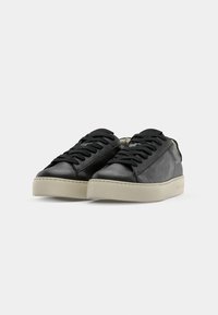 Paire de baskets basses en cuir noir avec lacets noirs et semelles épaisses en caoutchouc écru sur fond blanc.