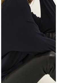 Navy oversized sweater made of soft fabric with wide sleeves, paired with fitted black leather pants. No visible patterns or hardware.