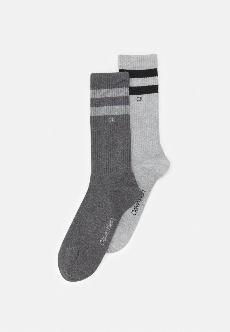 Due paia di calzini a costine, uno grigio scuro con due strisce e uno grigio chiaro con una striscia nera, entrambi con il logo "Calvin Klein" alla caviglia.
