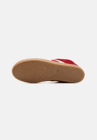 Såle av en rød sukkersneaker med sirkulært sko-dekk mønster og "Lagd i Italia" merket på den lysebrune gummisålen.