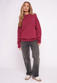 Różowy sweter dziany o luźnym kroju z opuszczonymi ramionami, zestawiony z szarymi dżinsami i białymi trampkami z beżowymi akcentami.