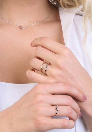 Silver rings displayed on two fingers, one with a smooth band and the other featuring a zigzag design. Simple, polished finish.
