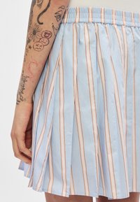 Jupe plissée bleue avec des rayures alternées rose et blanches, dotée d'une taille élastique et d'une texture de tissu douce et lisse.