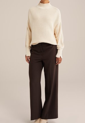 Knitted cream turtleneck sweater with wide sleeves, paired with black high-waisted trousers. Smooth texture, relaxed fit, and ankle-length hem.