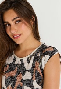 Top de manga corta con un patrón de camuflaje en negro, beige y marrón, con cuello redondo y un acabado de tela texturizada.