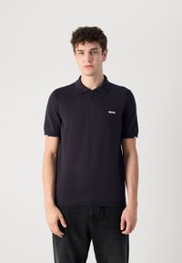 Ναυτικό μπλε polo με κλείσιμο με φερμουάρ, κοντά μανίκια, ριγωτό στρίφωμα, με μικρό λευκό λογότυπο "BOSS" στο αριστερό στήθος. Λείο πλέγμα υφής.